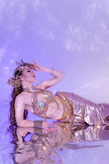 Elizabeth Khard reclining in a gold costume against a lavender sky