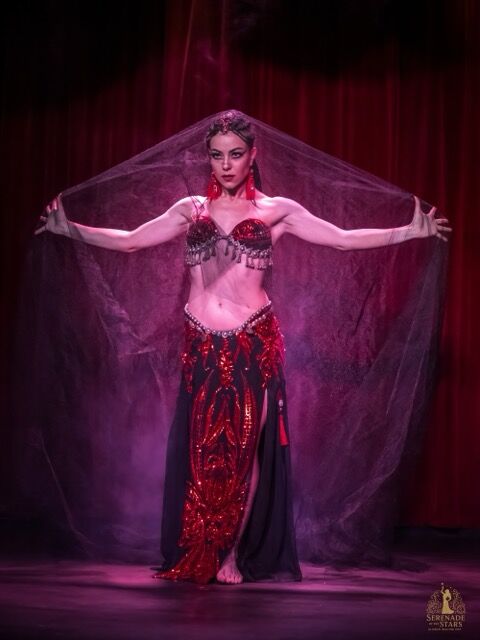Elizabeth Khard performing with a veil on stage in red light