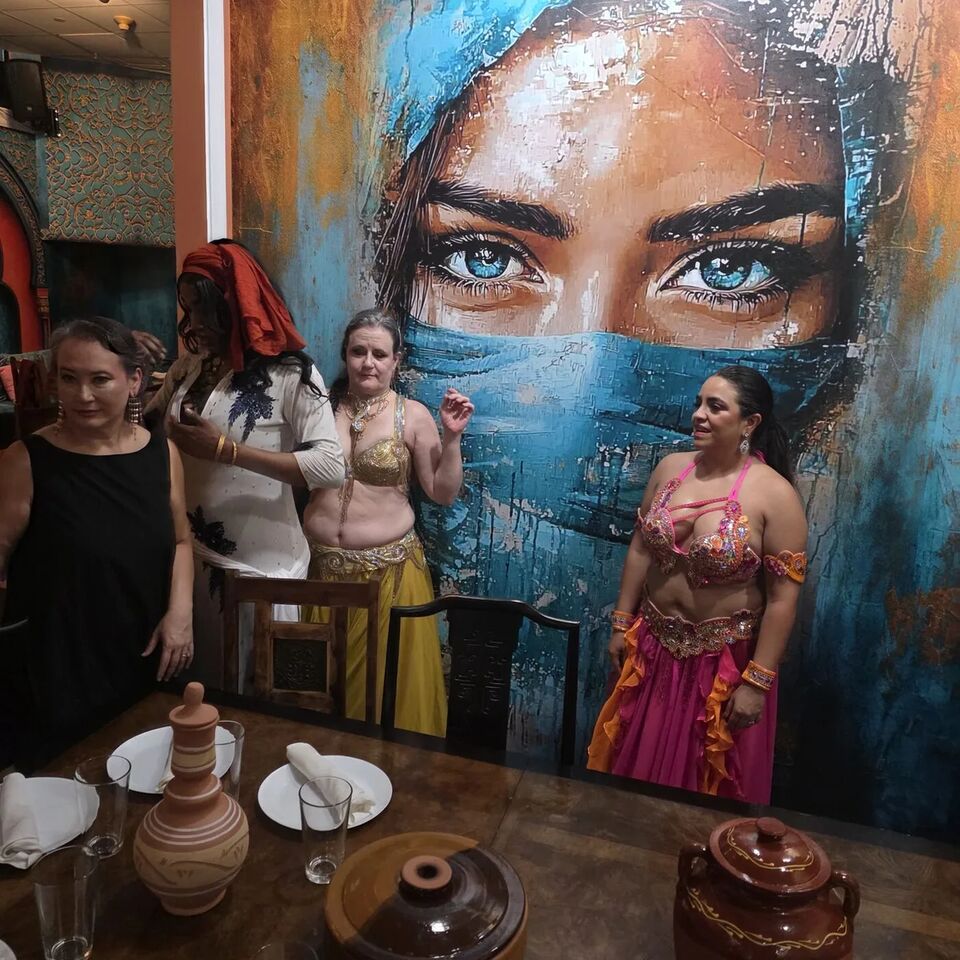 Two dancers in costume in front of the mural at the July Hafla