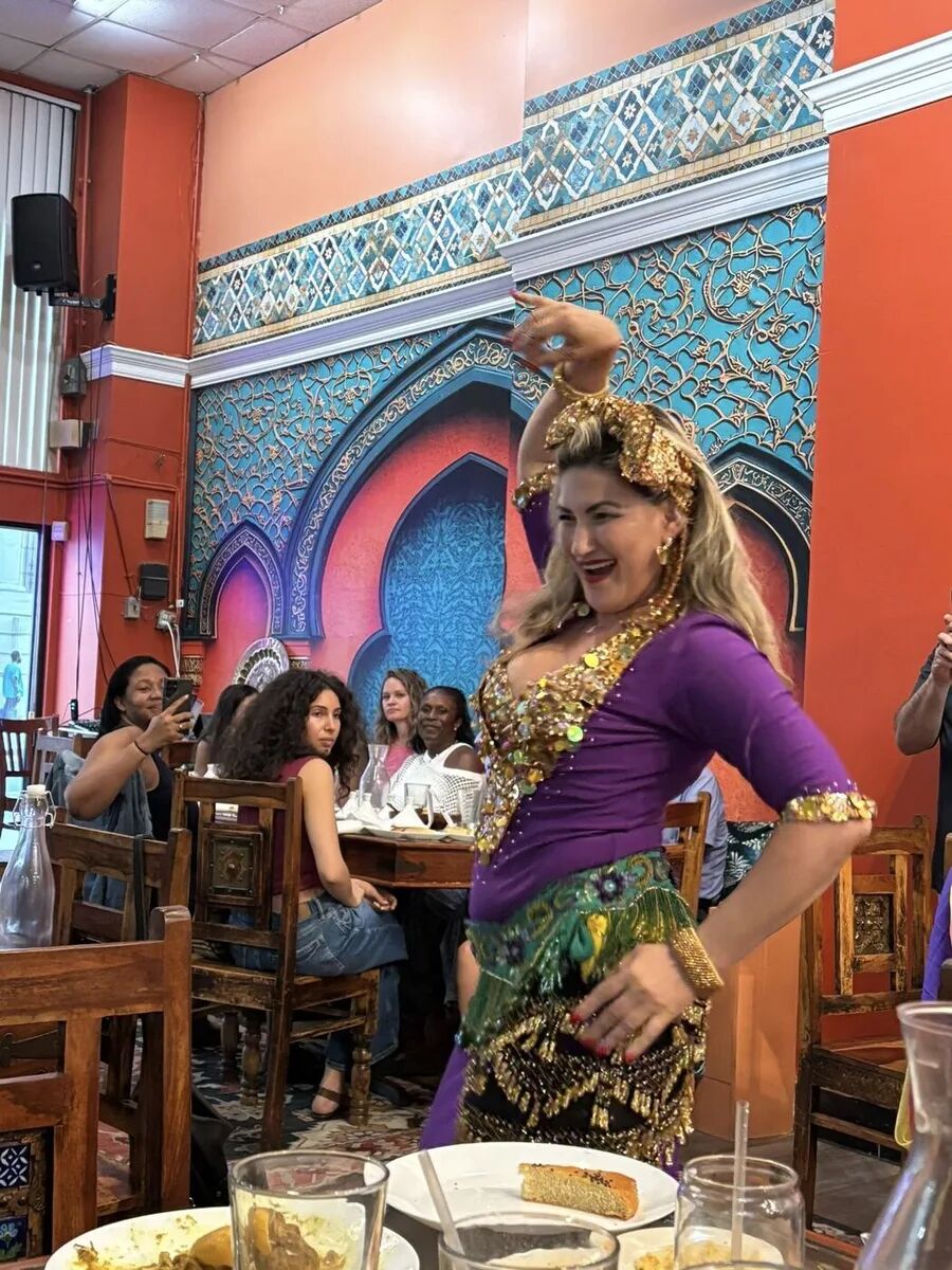 Dancer in purple and gold posing before the arch at the inaugural Hafla
