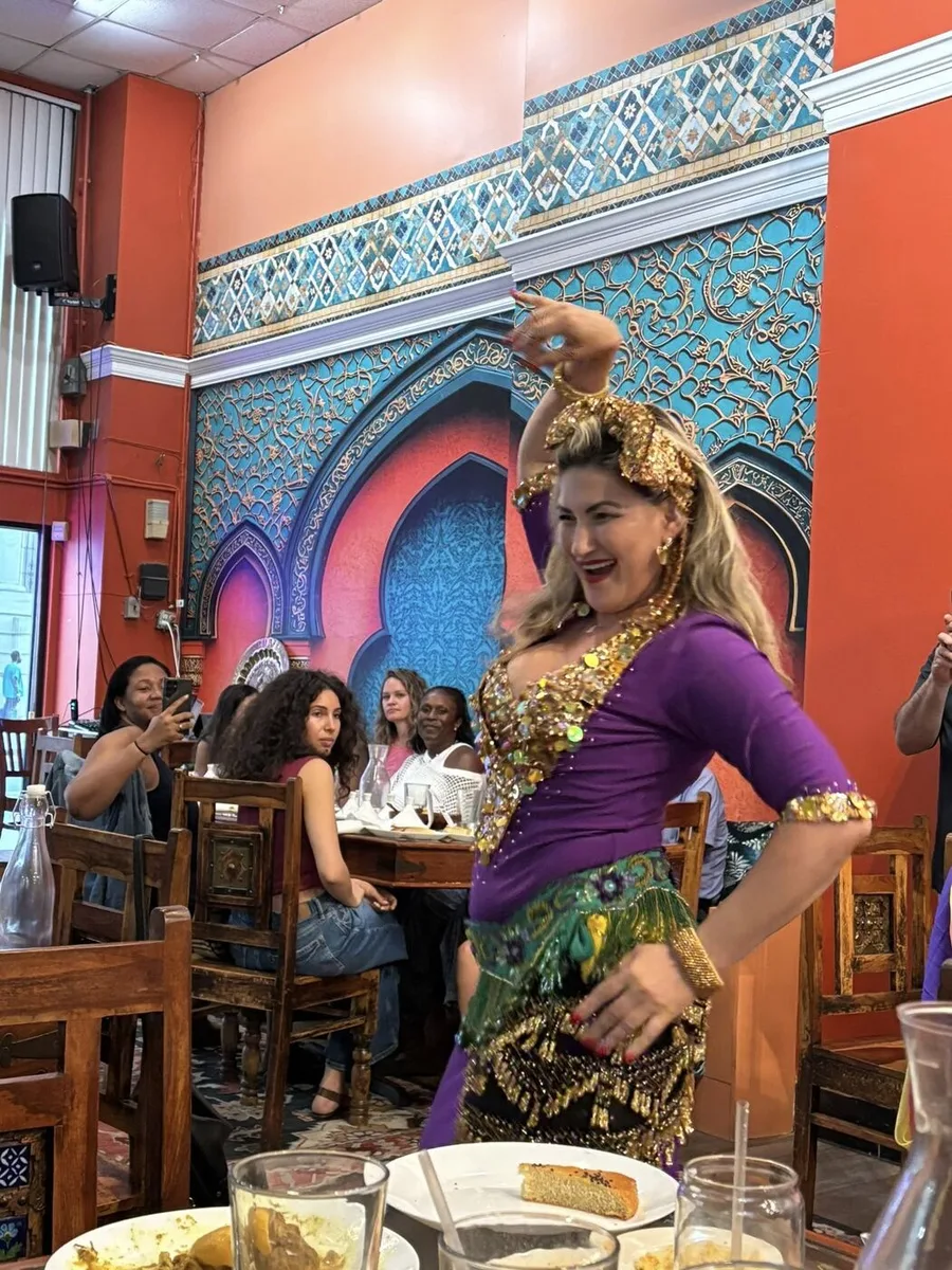 Dancer in purple and gold posing before the arch at the inaugural Hafla