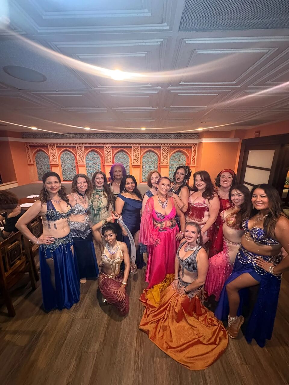 The full September lineup posing together under the arches, one dancer kneeling in front with an orange veil spread across the floor
